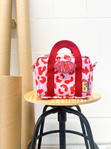 Tasche aus Kunstleder mit Leoprint in rosa und rot, die auf einem, Hocker steht